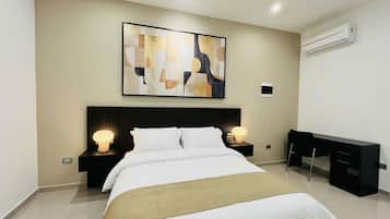A modern hotel room with a bed, bedside lamps, a desk, and an abstract painting on the wall.