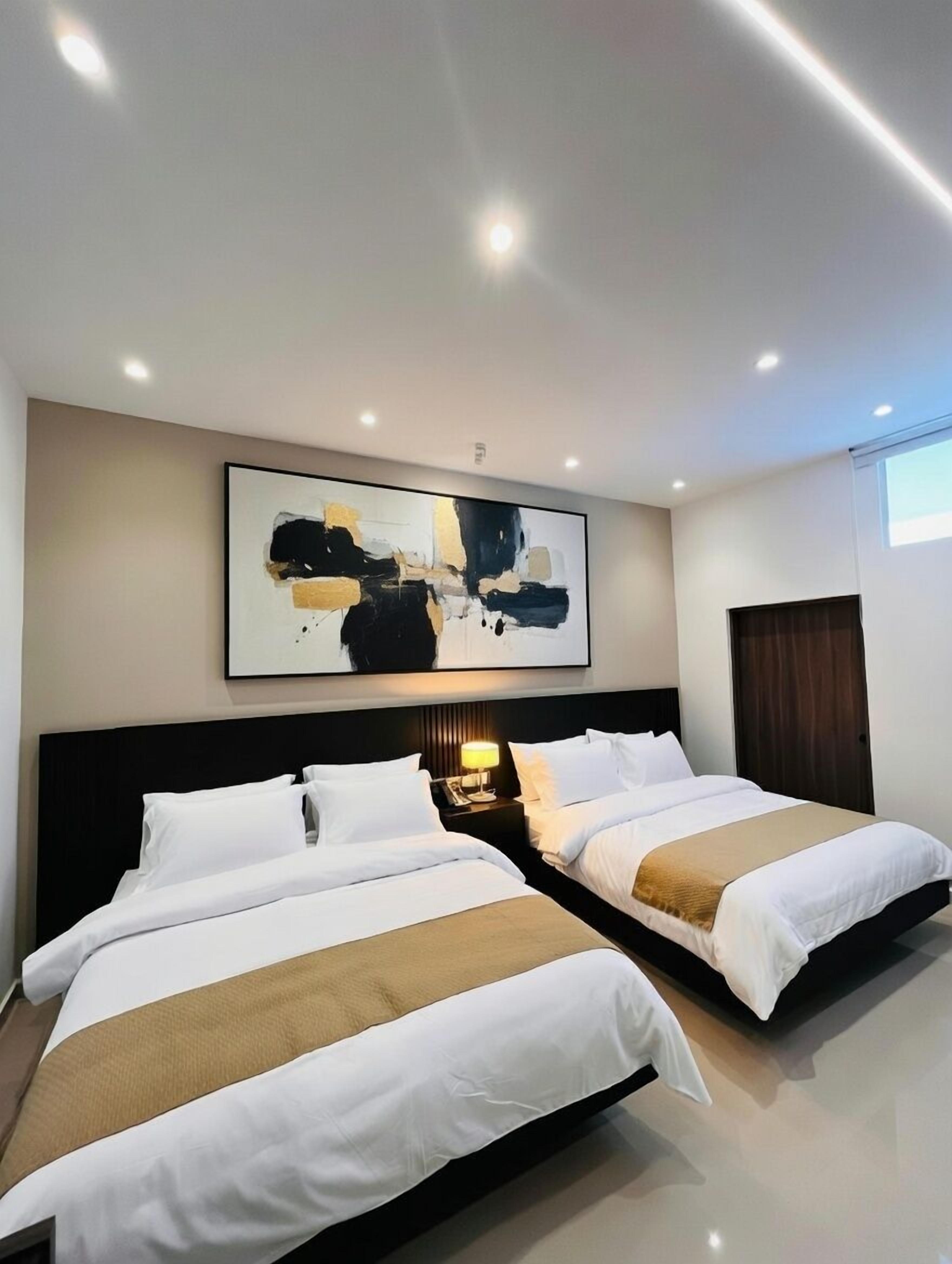 Une chambre d’hôtel avec deux lits, une grande peinture abstraite au mur et une table de chevet avec une lampe.