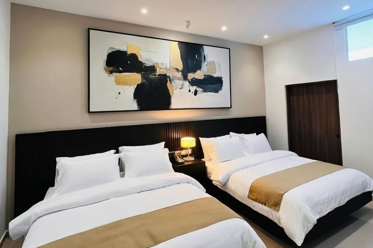 Ein Hotelzimmer mit zwei Betten, einem großen abstrakten Gemälde an der Wand und einem Nachttisch mit einer Lampe.