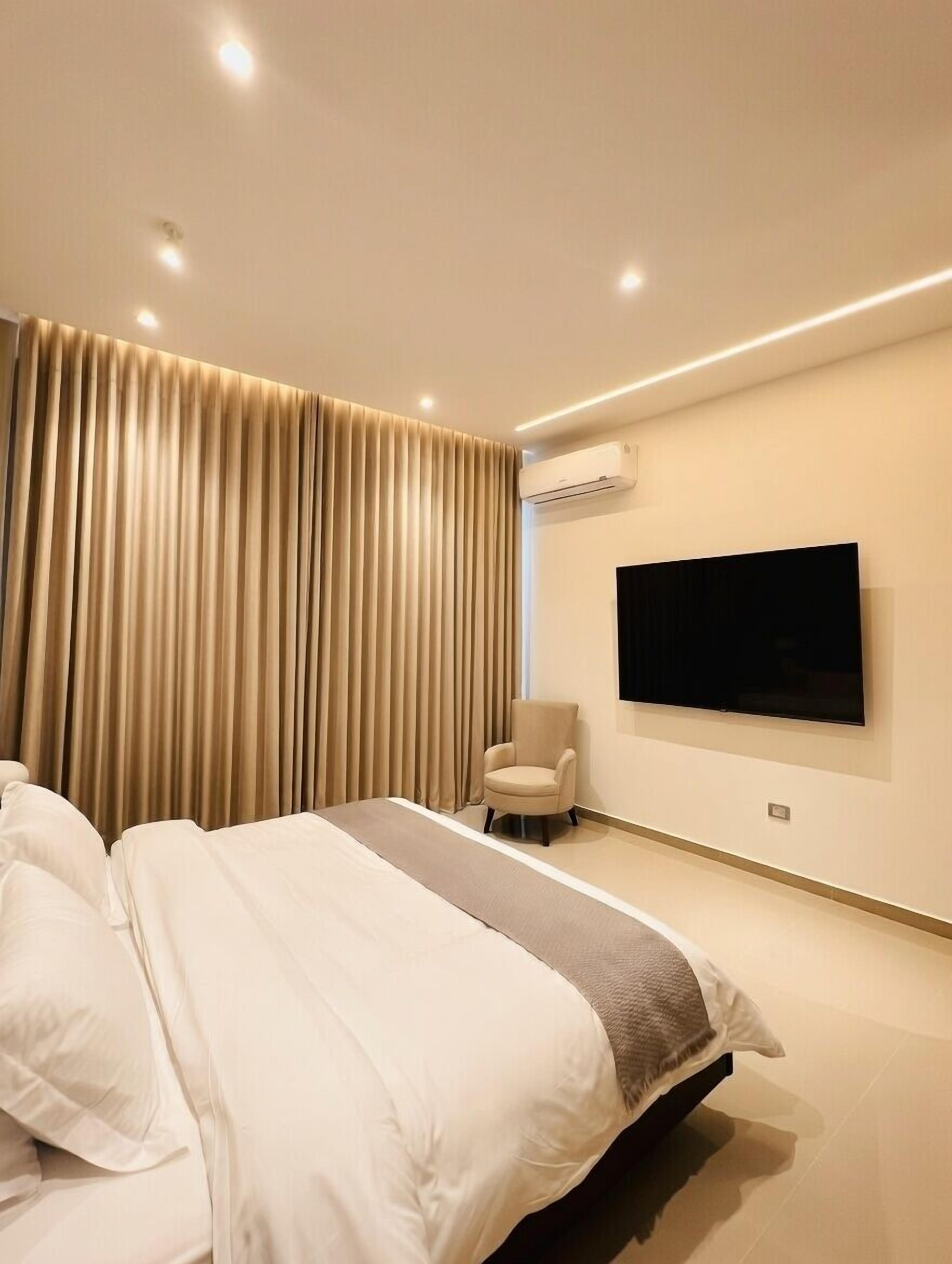 Une chambre moderne avec un grand lit, un téléviseur à écran plat fixé au mur et un appareil de climatisation.