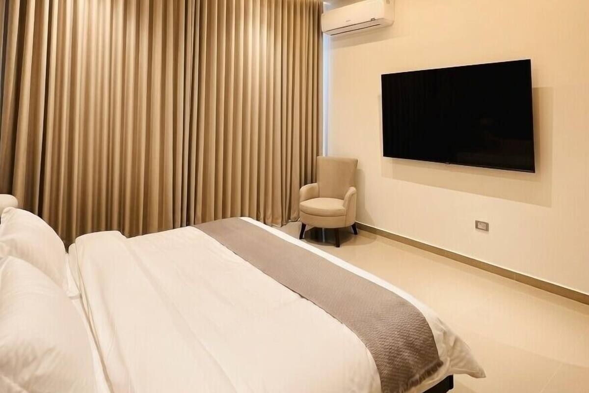 Ein modernes Schlafzimmer mit einem großen Bett, einem flachbildfernseher an der Wand und einer Klimaanlage.