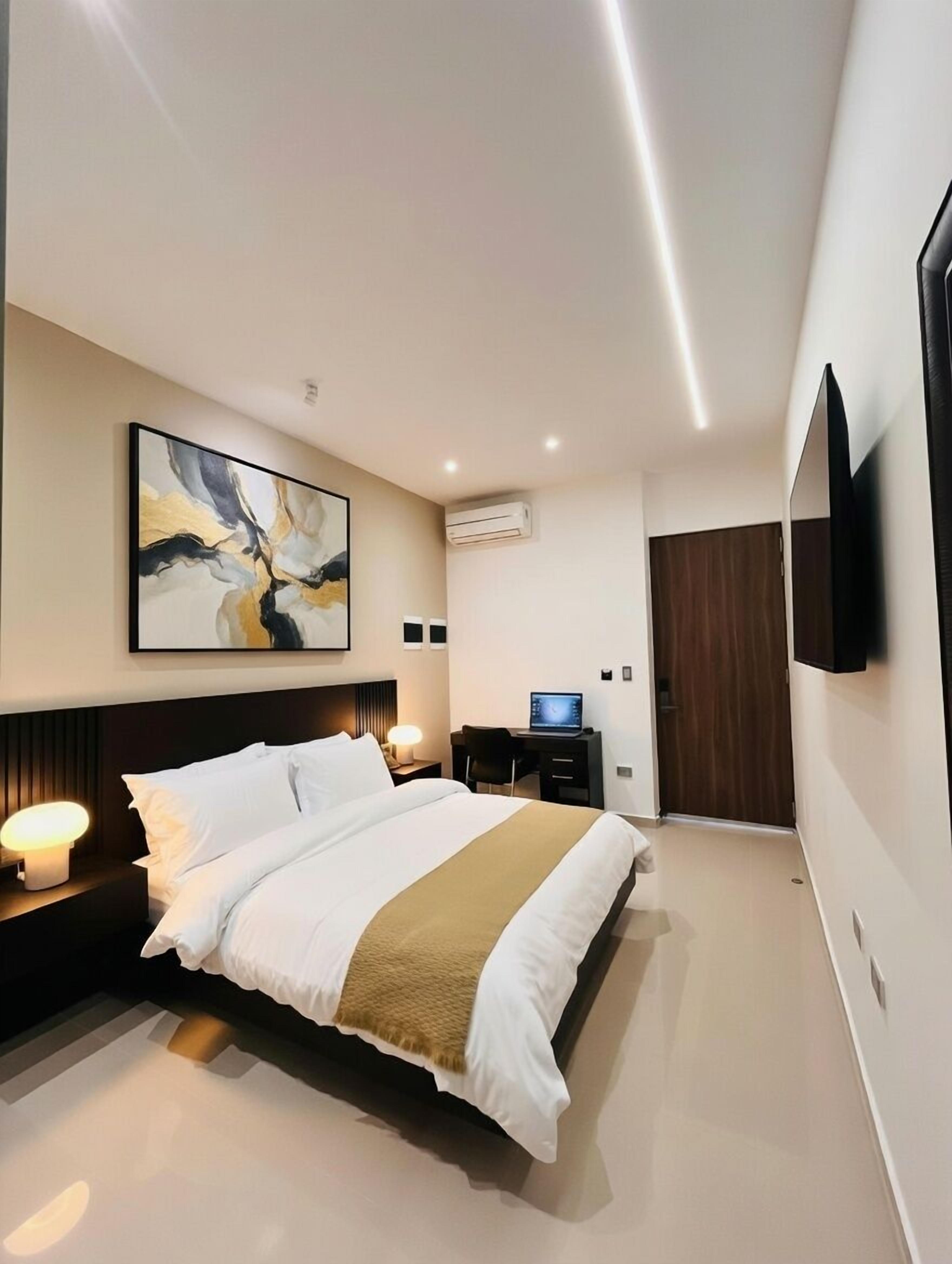 Une chambre d’hôtel moderne dotée d’un grand lit, d’un bureau avec un ordinateur portable, d’une télévision à écran plat et d’un système de climatisation.