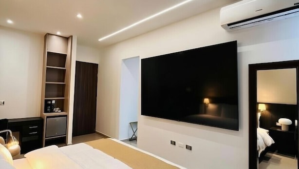 Une chambre d’hôtel moderne avec un grand lit, un téléviseur fixé au mur, une armoire et une table de chevet.
