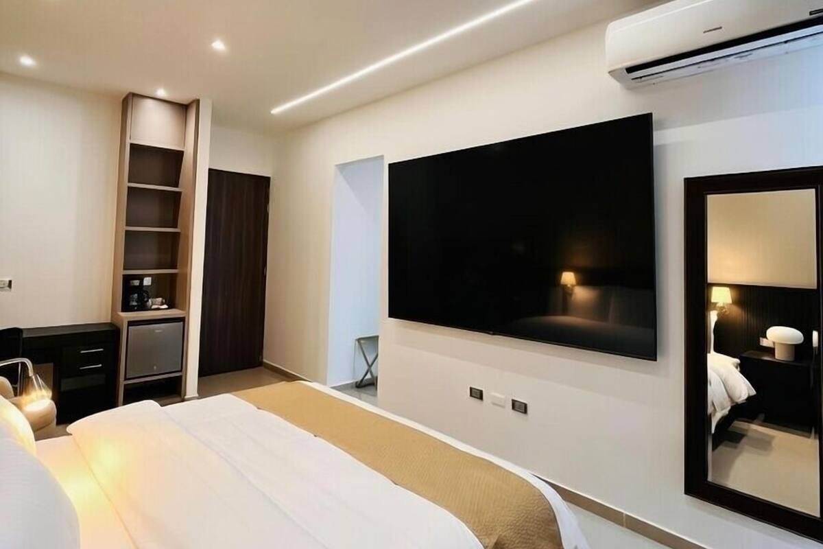 Ein modernes Hotelzimmer mit einem großen Bett, einem an der Wand befestigten Fernseher, einem Kleiderschrank und einem Nachttisch.