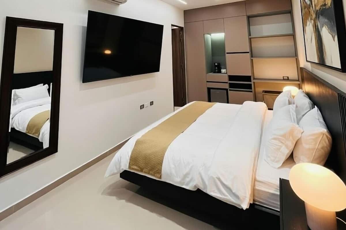 Ein modernes Hotelzimmer mit einem großen Bett, einem Flachbildfernseher, einem Spiegel, einem Nachttisch mit Lampe und einer wandmontierten Klimaanlage.