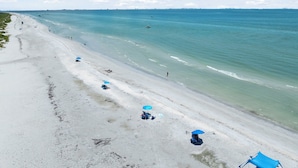 Een strand met helder turquoise water, wit zand en enkele mensen en parasols.