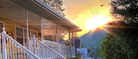 Ein Haus mit Veranda und Blick auf einen Sonnenuntergang über einem bewaldeten Hügel.