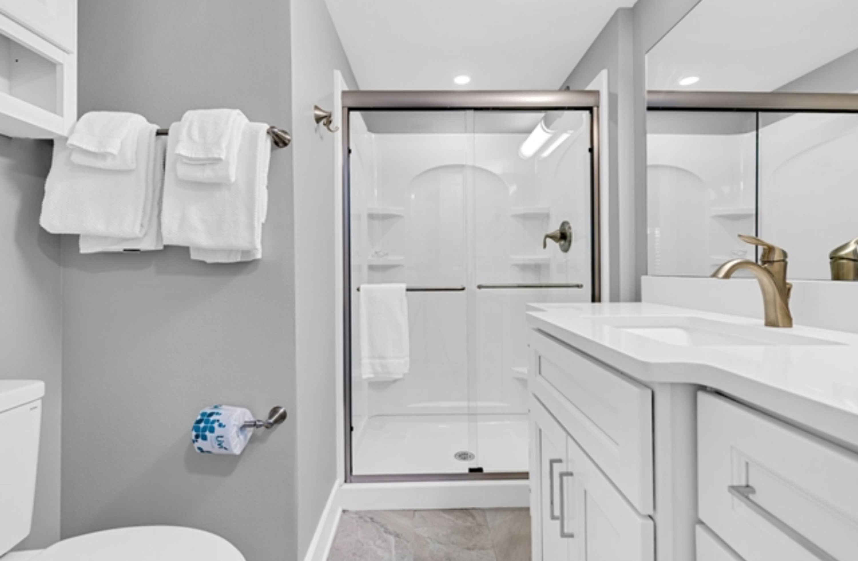 A modern bathroom with a glass-enclosed shower, white fixtures, and a marble floor.