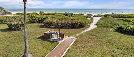 Ein Weg, der zu einem Strand mit einer Palme und einer kleinen Sitzgelegenheit führt.