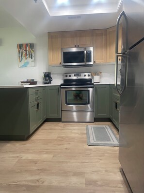 A modern kitchen with green cabinets, stainless steel appliances, and a wooden floor. - Steps to Park City Ski Lifts - Hot Tub - Sleeps 4 (Park City)