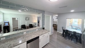 Una cocina moderna con encimeras de granito, lavavajillas y un comedor con mesa y sillas.
