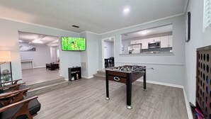 Una sala de estar moderna con una mesa de fútbol de mesa, un televisor de pantalla plana y una cocina al fondo.