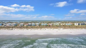 En kustutsikt med fastigheter som ligger vid stranden, en sandstrand och vågor som bryter mot havet.