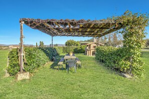 Un jardin agrémenté d’une pergola en bois, d’une table avec des chaises et d’un petit bâtiment en arrière-plan.