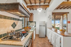 A kitchen with a gas stove, a refrigerator, and a view of the outside. - Casale Le Sorgenti - Farmhouse with Pool for 8, Pitigliano, Italy (Pitigliano)