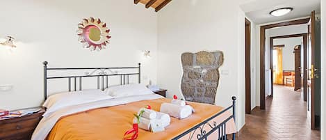 Habitación de hotel con una cama, vigas de madera en el techo, una pared de piedra y un pasillo que conduce a otra habitación.