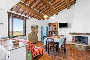 A rustic dining area with a stone wall, wooden ceiling beams, a fireplace, and a television mounted on the wall. - Sorgenti Pitigliano 2 with Shared Pool and Terrace, Pitigliano, Italy (Pitigliano)