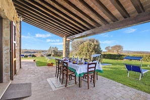 Eine Terrasse im Freien mit Esstisch, Stühlen und einer Pergola darüber.