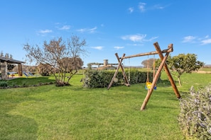 Eine grüne Rasenfläche mit einer Holz-Schaukel und einem Steinhaus im Hintergrund.