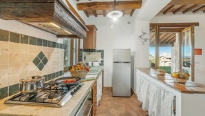 Cozinha equipada com fogão a gás, forno e frigorífico. Há cestas de fruta no balcão e uma janela com vista para o exterior.