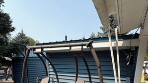 Eine Terrasse mit zwei grünen Sitzgelegenheiten und einem kleinen Holztisch, verbunden durch einen Metallrahmen.