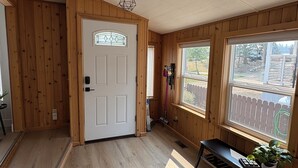 Ein Zimmer mit Holzwänden und einer weißen Tür, großen Fenstern und einer Bank mit einer Pflanze.