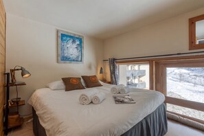 A hotel room with a large bed, a painting on the wall, and a view of a snowy landscape through the window. - Grand Roc B118 260m from Slopes, View, Parking & WiFi, Argentière (Chamonix), France (Argentière (Chamonix))