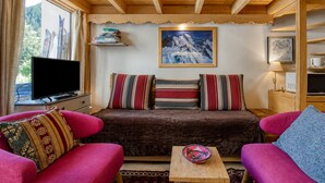 Une pièce chaleureuse avec un plafond en bois, un canapé agrémenté de coussins à rayures, un téléviseur et un tableau encadré représentant une montagne.