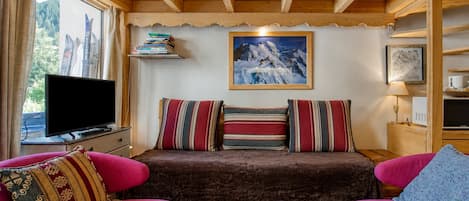 A cozy room with a wooden ceiling, a sofa with striped cushions, a television, and a framed picture of a mountain.