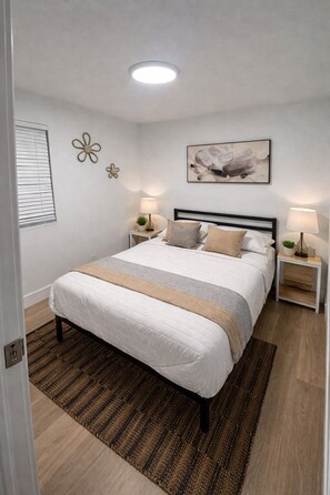 Une chambre à coucher bien rangée, avec un lit, deux tables de chevet, une lampe fixée au mur et un luminaire au plafond.