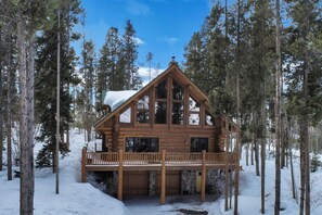 Una cabaña de madera con balcón, rodeada de altos pinos y nieve.