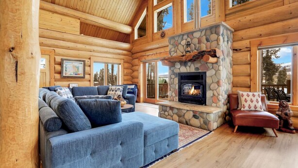 A log cabin interior with a stone fireplace, a blue sofa, and a red armchair.