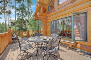 Une terrasse en bois avec une table ronde et des chaises, entourée d’une balustrade en bois.