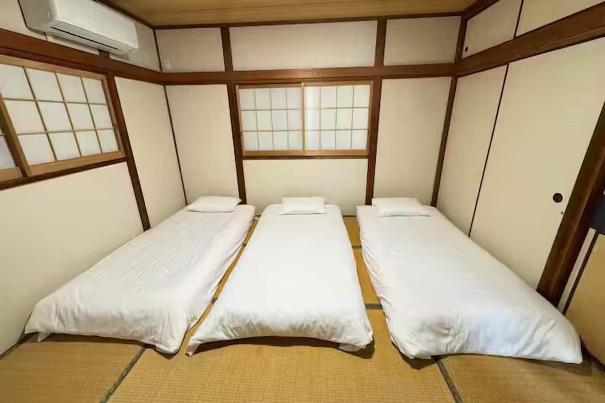 Una habitación con tres camas individuales, suelo de tatami, puertas correderas y aire acondicionado instalado en el techo.
