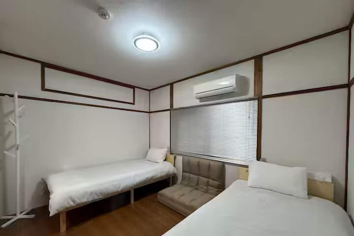 Una habitación con dos camas, un banco, un aire acondicionado y una ventana con persianas.