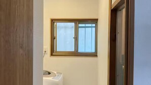 Un pasillo estrecho con una ventana, una lavadora y una puerta.
