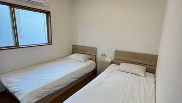 A small, clean room with two single beds, a window, and a ceiling light fixture.