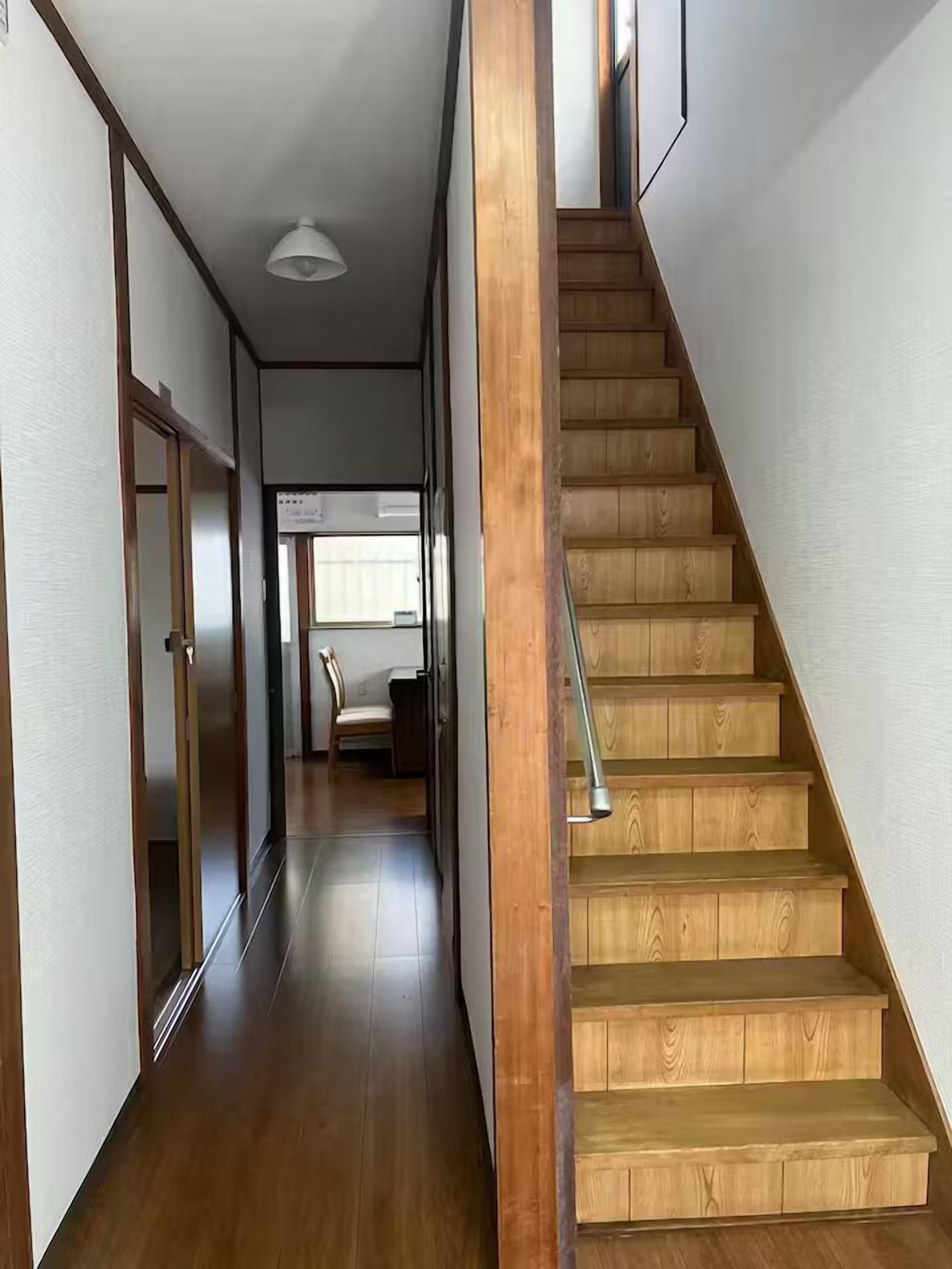 A wooden staircase leading to a room with a desk and chair, a ceiling light, and a view of a window.