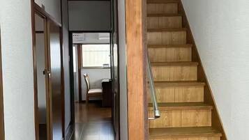 A wooden staircase leading to a room with a desk and chair, a ceiling light, and a view of a window.