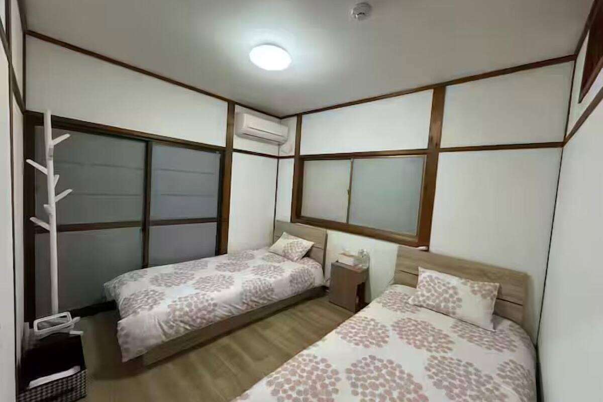 Un dormitorio con dos camas, una mesita de noche, una lámpara y una ventana.