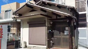 Edificio japonés tradicional con una persiana cerrada, un pequeño portón de entrada y un equipo de aire acondicionado visible.