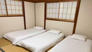 Una habitación tradicional japonesa con suelo de tatami, dos camas individuales con ropa blanca y ventanas con puertas shoji.
