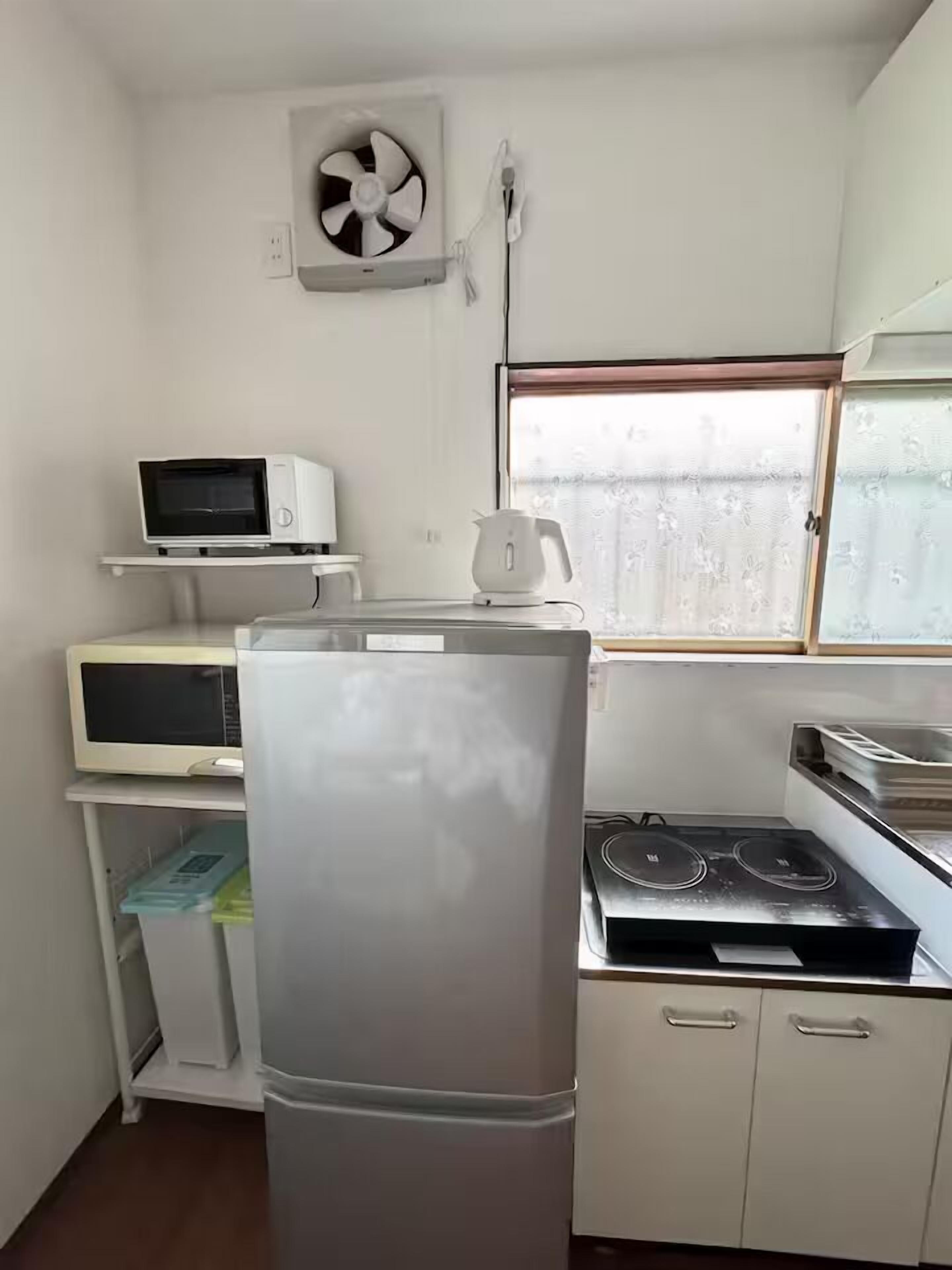 A compact kitchen with a refrigerator, microwave, stove, and a fan.