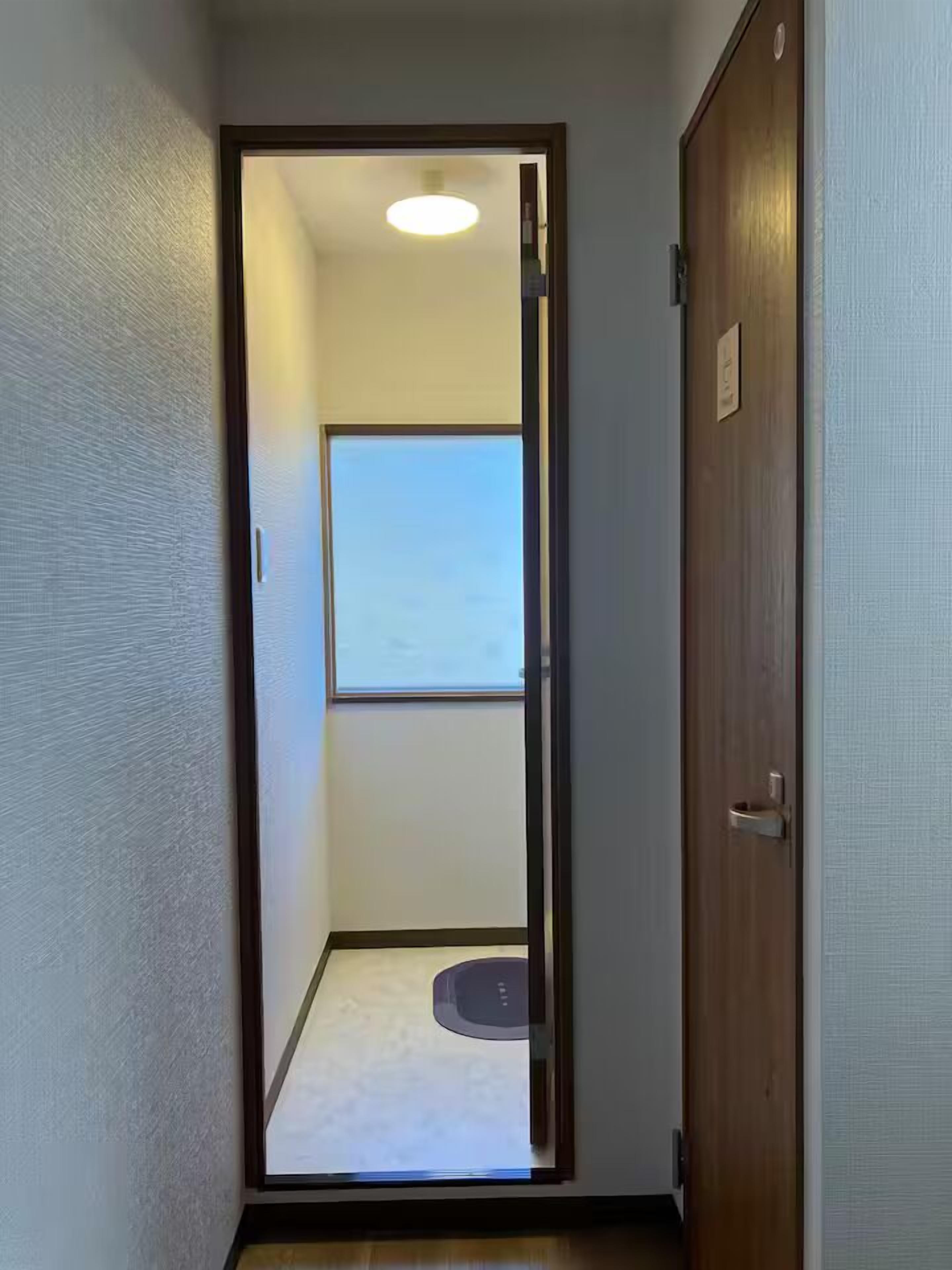 A narrow hallway with a wooden door on the right and a window on the left.