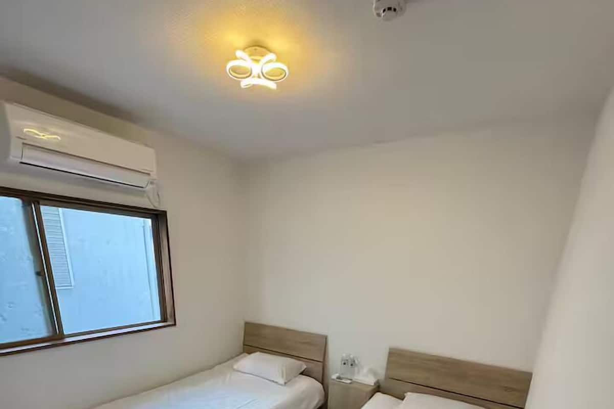 Una habitación pequeña y limpia con dos camas individuales, una ventana y una lámpara en el techo.