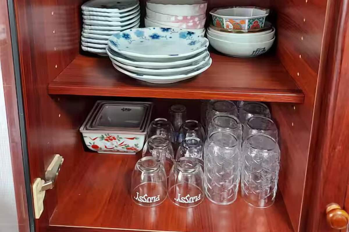 Un armario de madera con estantes que contienen cuencos, platos y cristalería blancos.