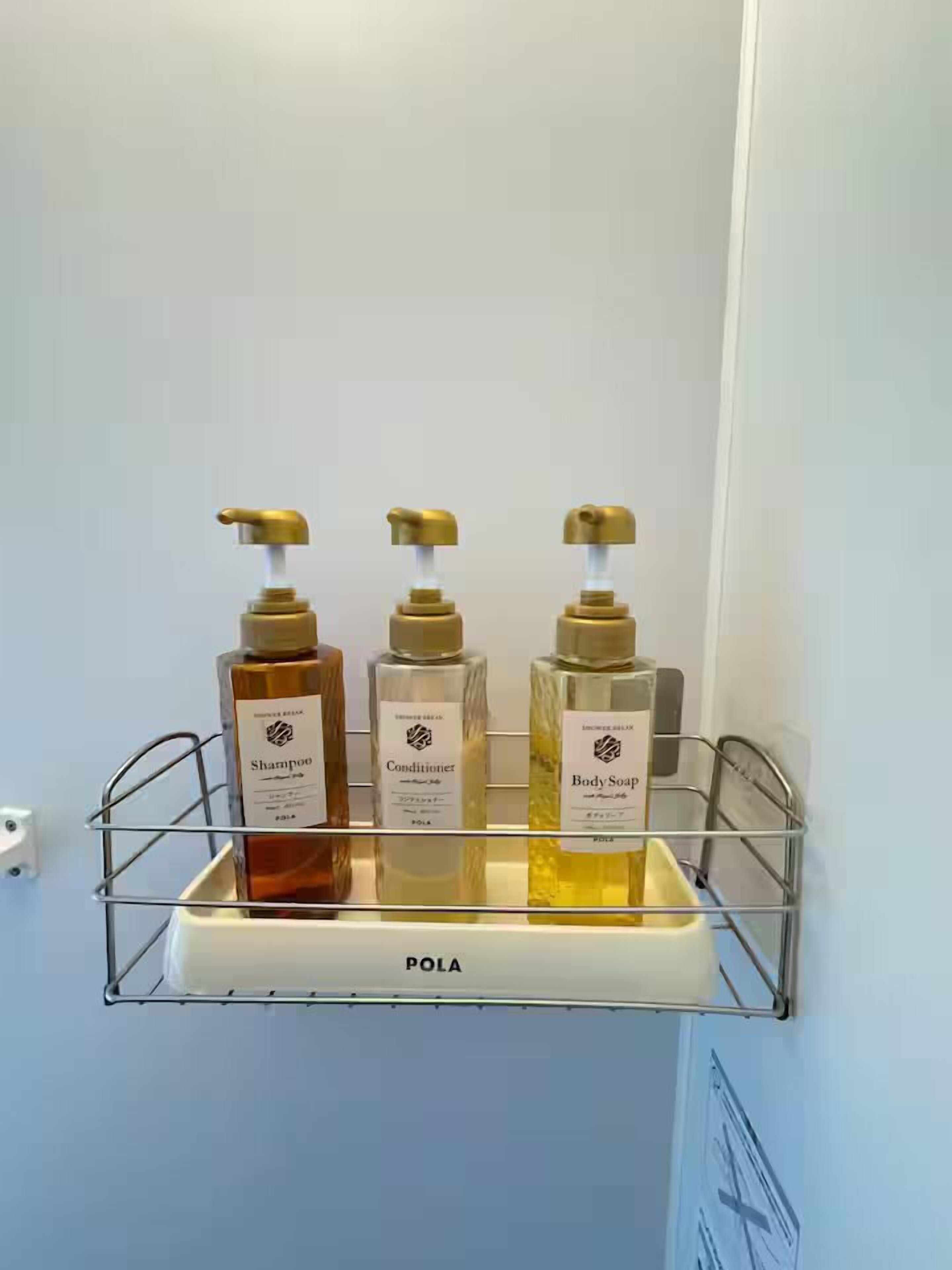 A bathroom shelf with three bottles of shampoo, conditioner, and body soap.