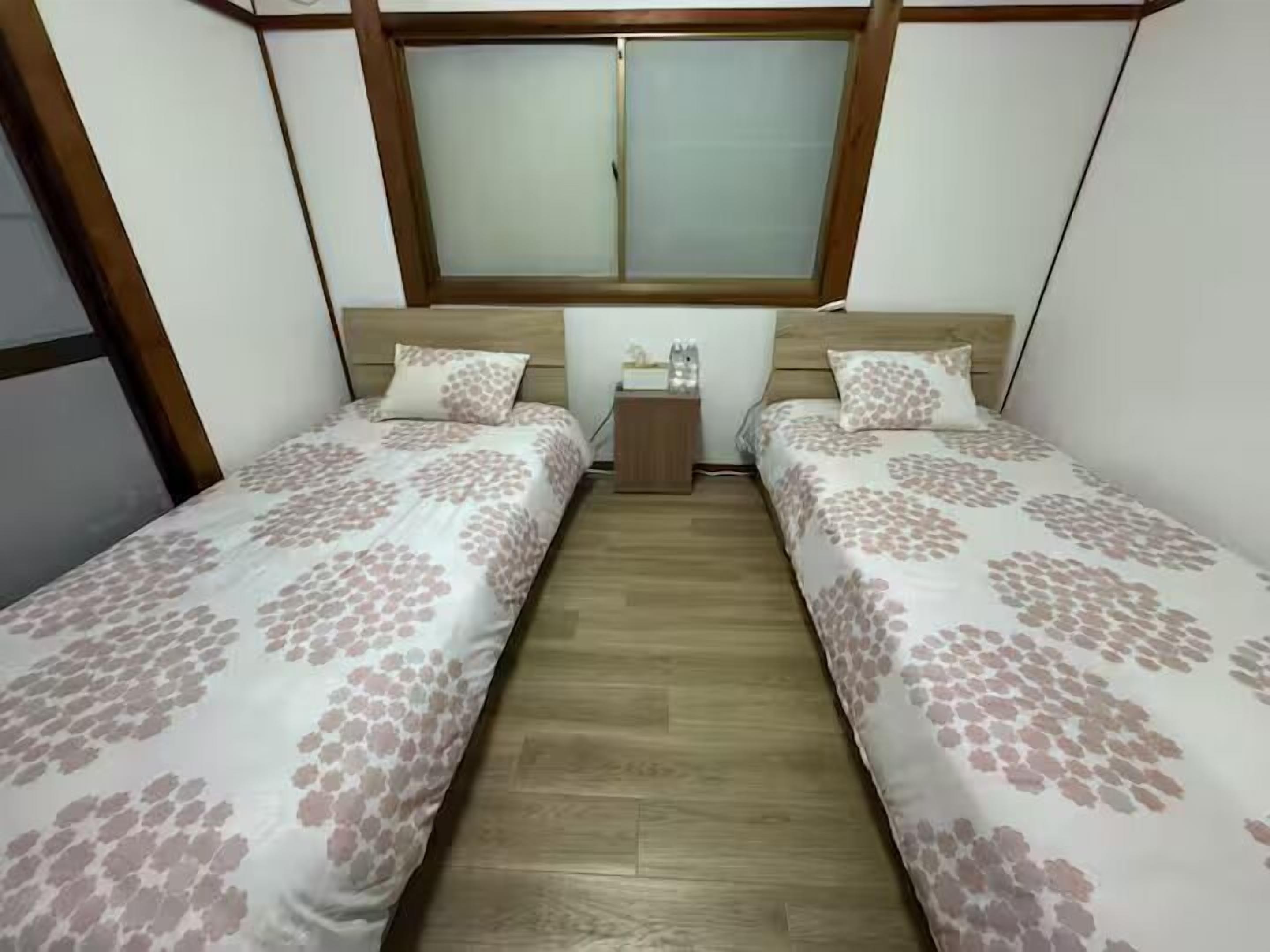 A small, clean room with two single beds, a nightstand, and a window.