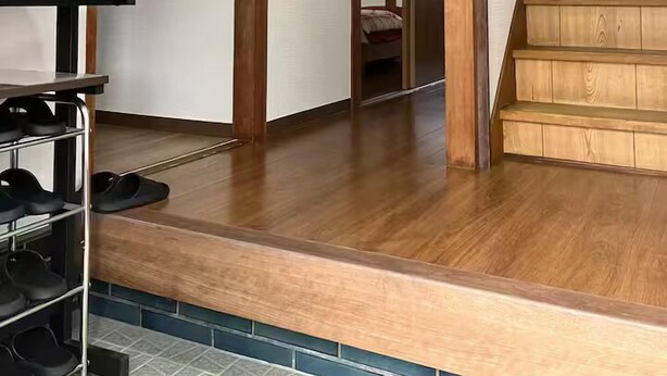 Un pasillo con una escalera de madera, un zapatero y una puerta que da a otra habitación.