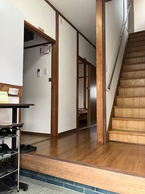 Un pasillo con una escalera de madera, un zapatero y una puerta que da a otra habitación.